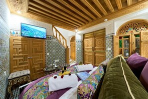 A traditional Moroccan room with a wooden ceiling, intricate tile work, a television, and a bed with colorful bedding. - Riad May Fes Original & Spa (Fès)