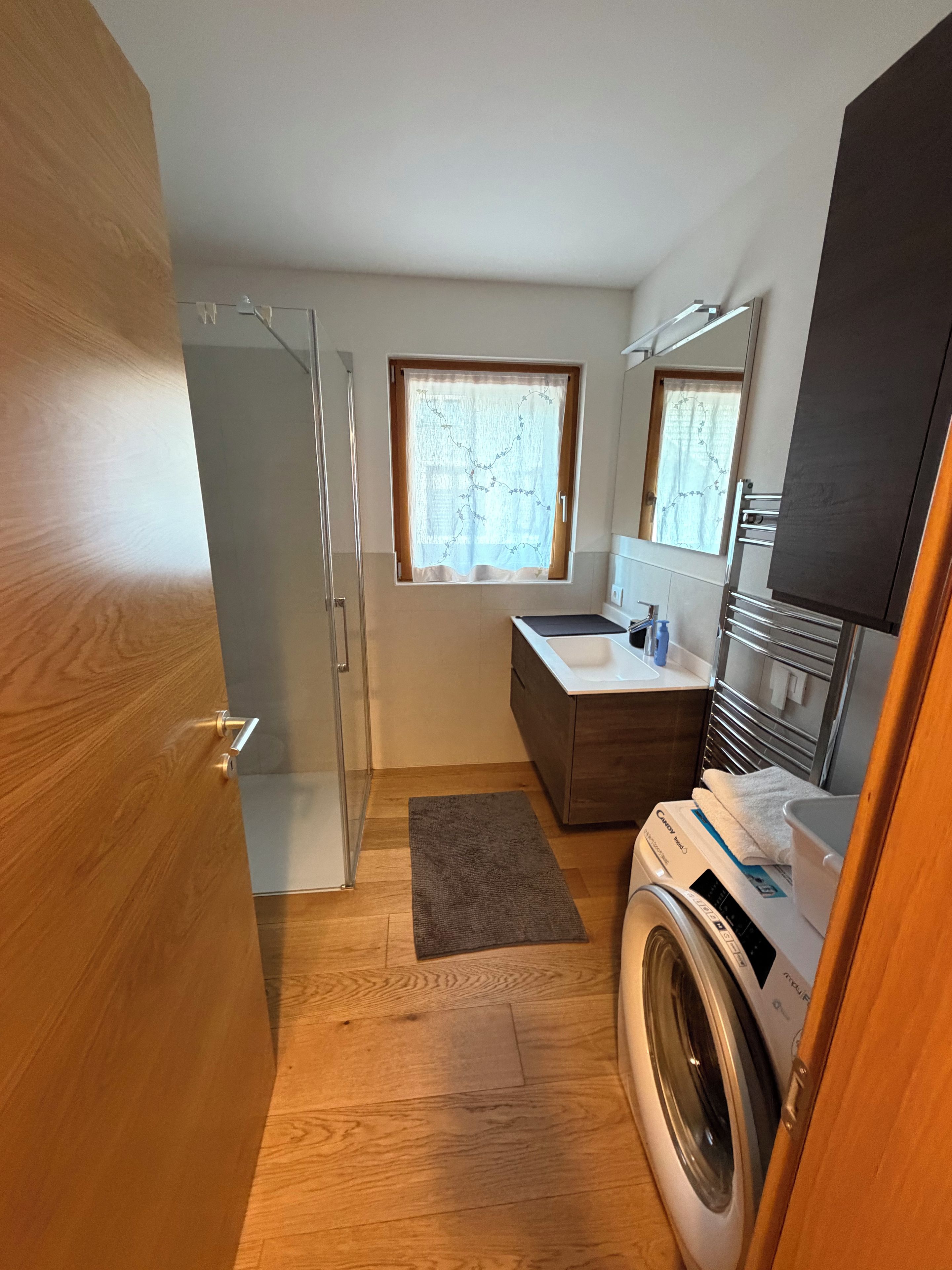 A compact bathroom with a washing machine, a sink, a mirror, and a shower.
