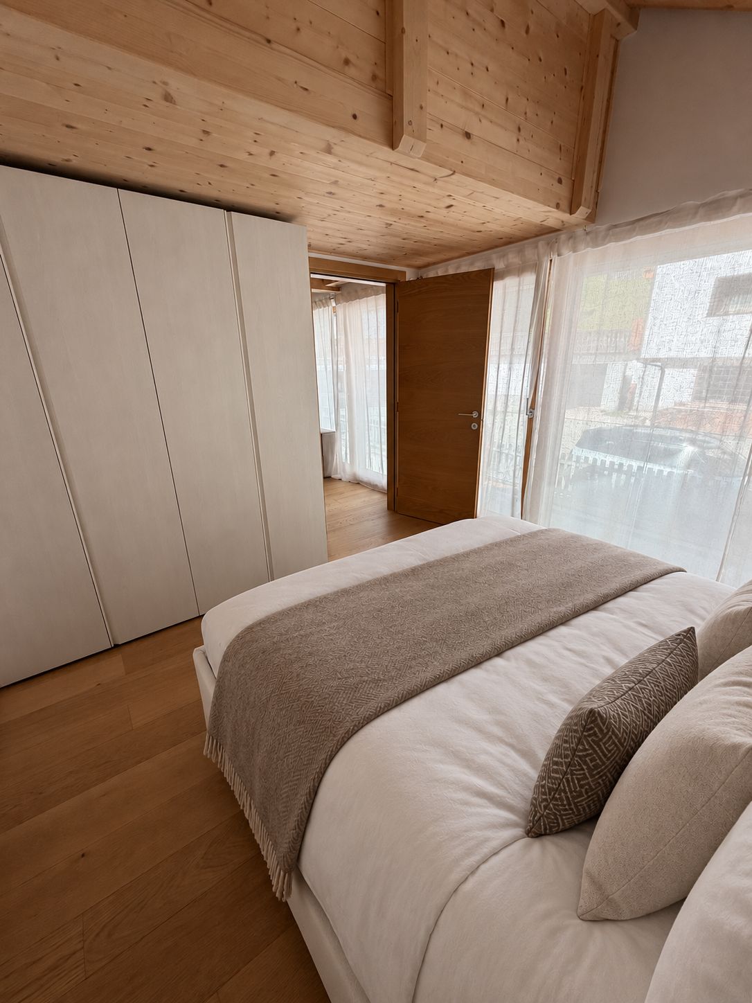 Une chambre avec un grand lit, un plafond en bois et une vue sur l’extérieur.