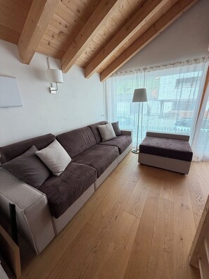 Ein modernes Wohnzimmer mit Holzboden, einem braunen Sofa, passendem Hocker und einer Stehlampe.