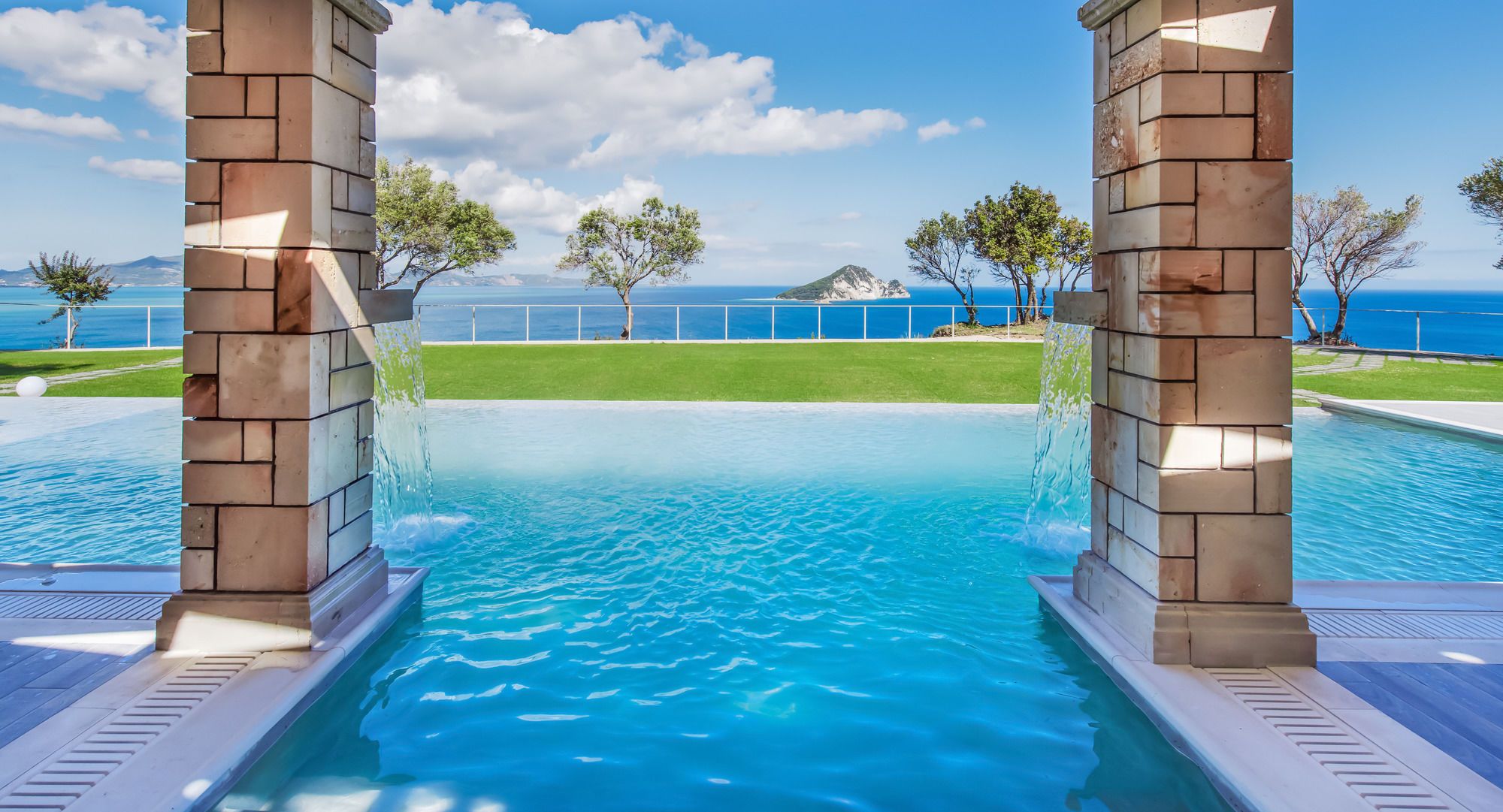 Una piscina con vistas al mar, rodeada de césped y árboles.