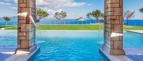 Una piscina con vistas al mar, rodeada de césped y árboles.