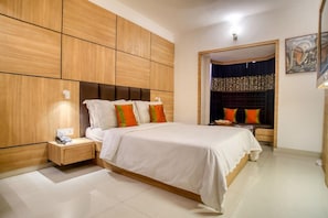 A modern bedroom with a large bed, wooden paneling on the walls, a nightstand, and a door leading to another room. - OYO Premium Rowland Road (Kolkata)
