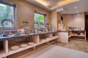 A buffet setup with multiple serving stations, a marble countertop, and a view of the outdoors through a window. - OYO Premium Rowland Road (Kolkata)