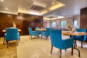 Un espace de restauration d’hôtel avec des chaises et des tables bleues, un téléviseur à écran plat fixé au mur et un mur recouvert de panneaux en bois.