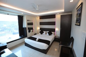 Una habitación de hotel moderna con una cama grande, un escritorio, una silla, un ventilador de techo y una ventana con vistas.