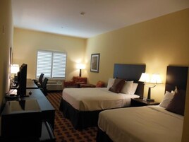 Habitación de hotel con dos camas, un escritorio, una silla y un televisor.