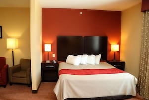 Una habitación de hotel con una cama grande, dos mesitas de noche, una silla y una lámpara.