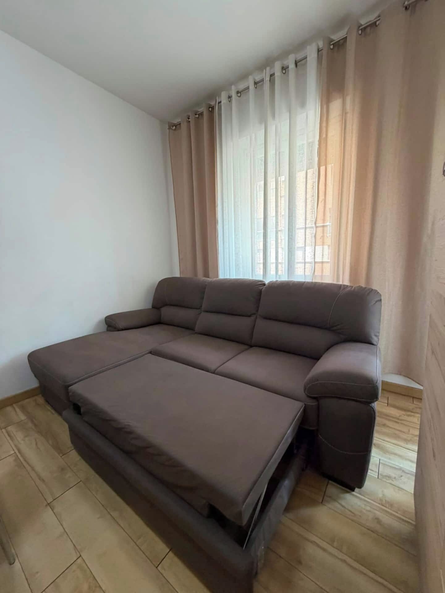 Una stanza con un divano letto, una finestra con tende e pavimento in legno.