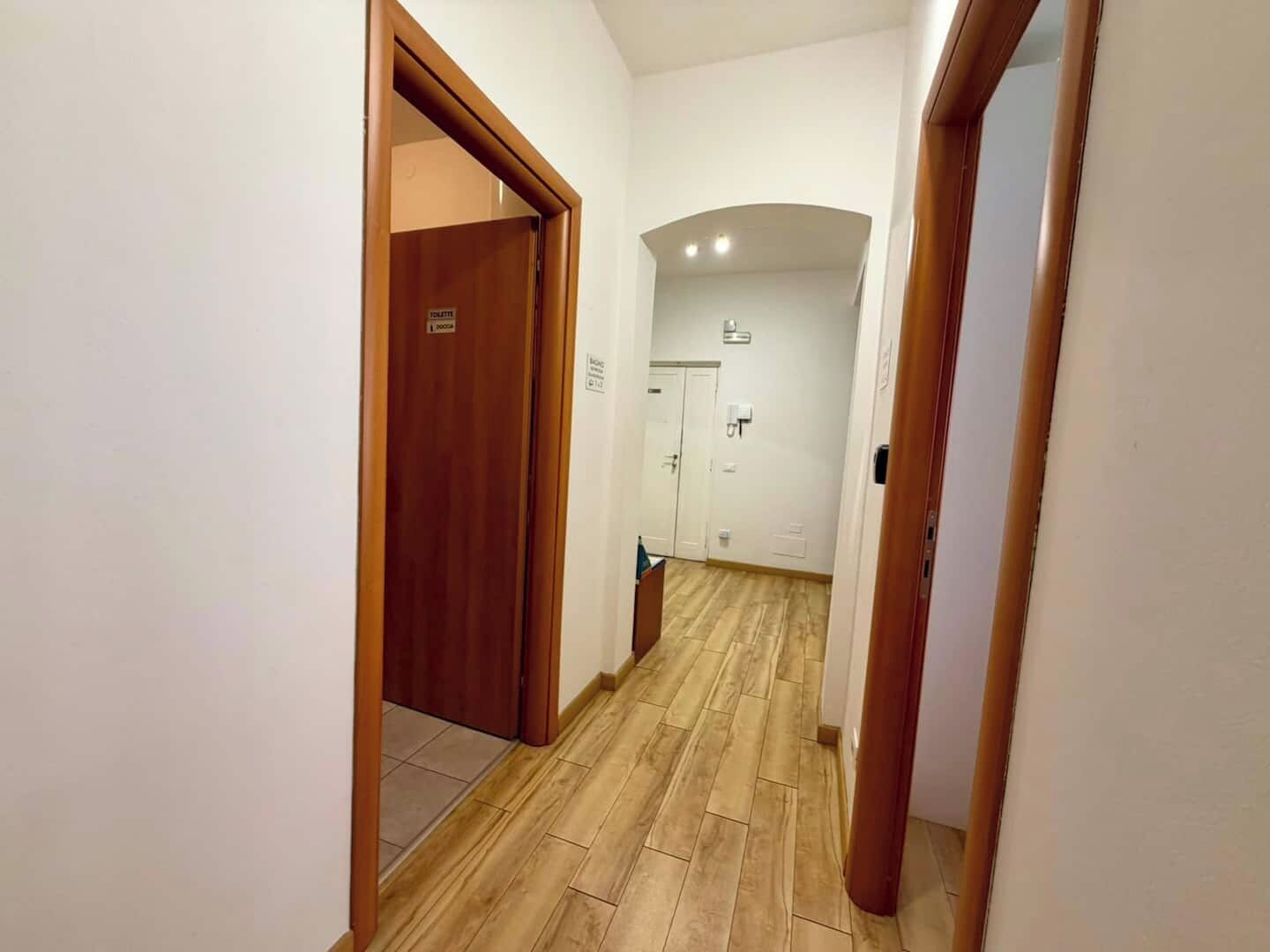 A hallway with wooden flooring, white walls, and a door labeled 'TOILETTE' leading to a bathroom.