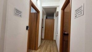 Un corridoio con porte in legno e cartelli che indicano 'Stanze Stanze 1 & 2' e 'Bagno Bagno Stanze/Stanze 1 & 2'.
