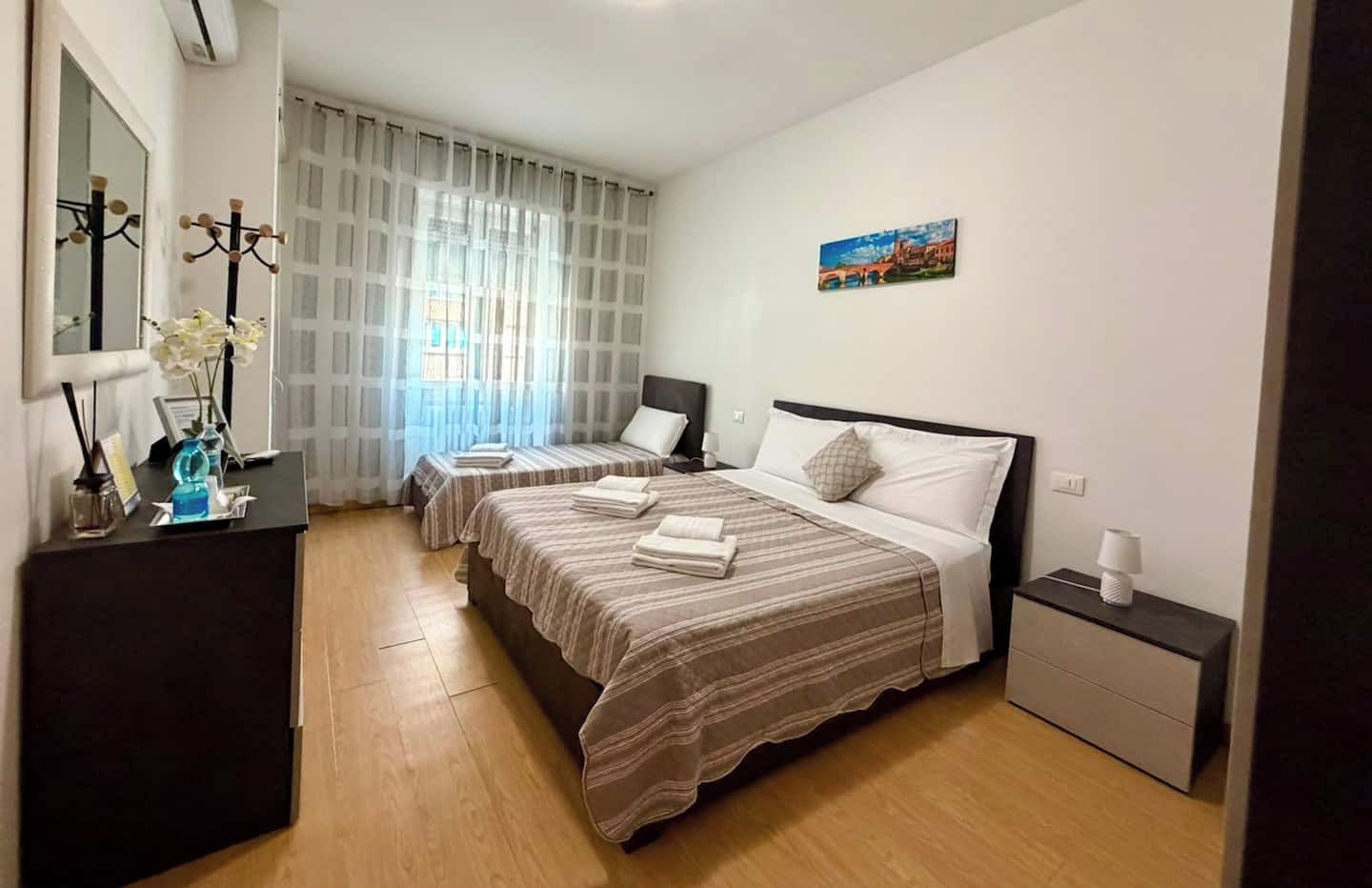 Camera d'albergo con due letti, una scrivania, una sedia, un comodino, una lampada e un quadro appeso al muro.