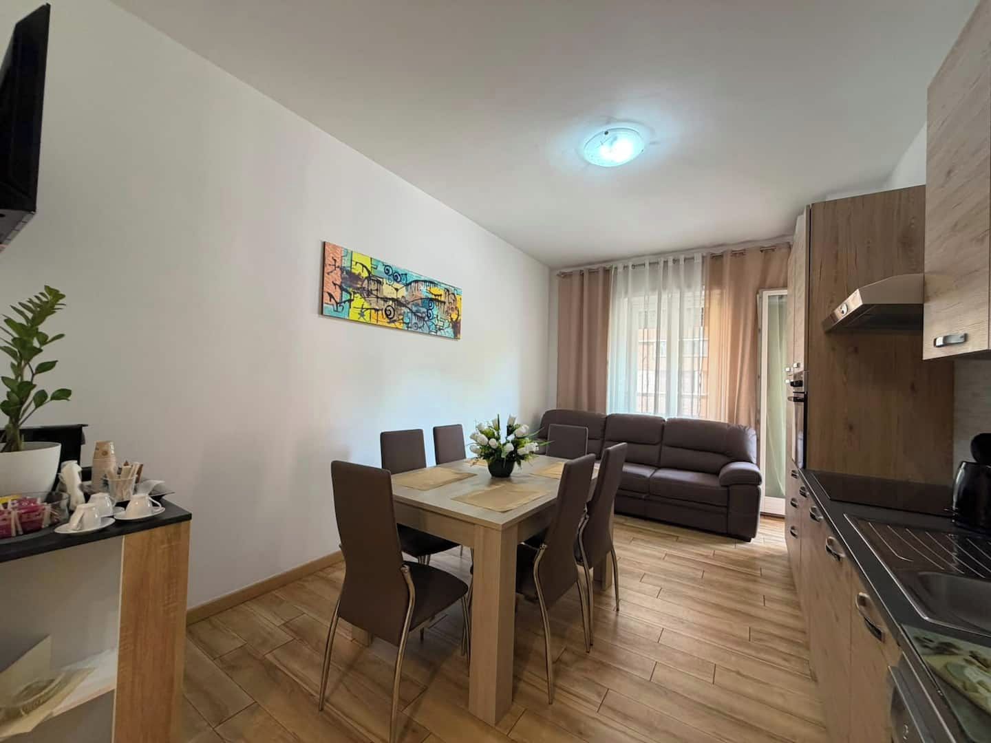 A modern living space with a dining area, a sofa, and a kitchen.