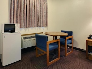 A small room with a microwave, a table with two chairs, a heater, and a curtain. - Americas Best Value Inn-winona/tyler (Tyler)