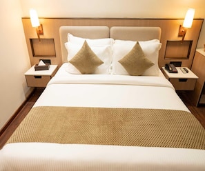Una habitación de hotel con una cama grande, dos mesitas de noche y dos lámparas fijadas a la pared.