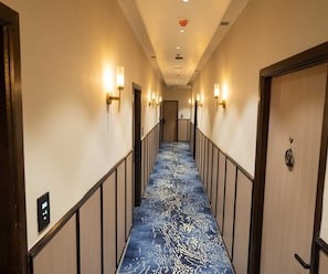 Un pasillo de hotel con alfombra azul estampada, luces empotradas en la pared y una puerta a la derecha.