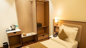 Quarto de hotel com cama, mesa de cabeceira, arm ário e pequena área de trabalho com chaleira e garrafas.