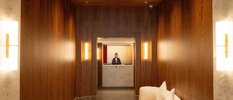A hotel reception area with a wooden interior, a reception desk, and two white armchairs.
