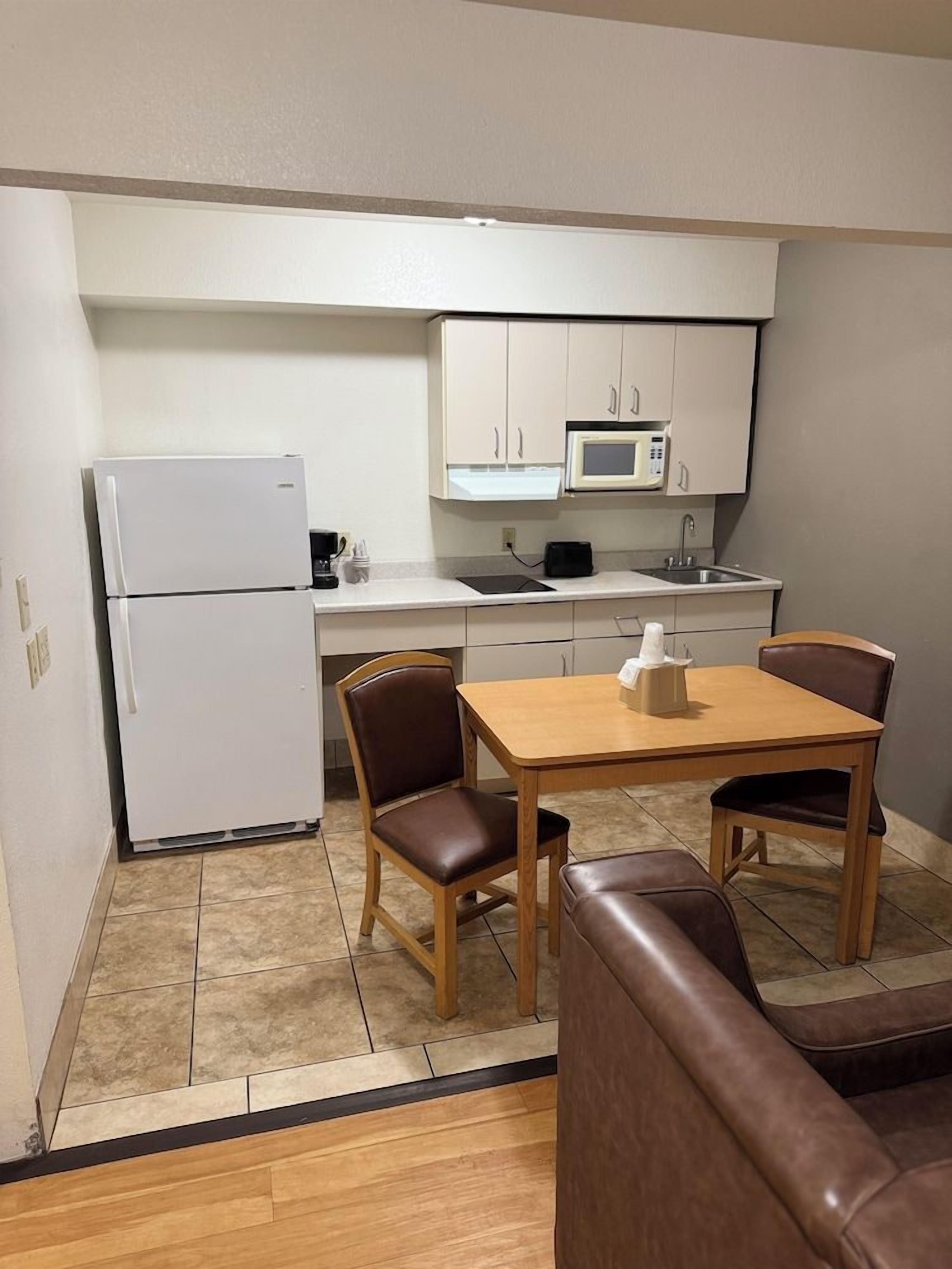 A compact kitchenette with a refrigerator, microwave, and sink. There is a small dining table with two chairs.