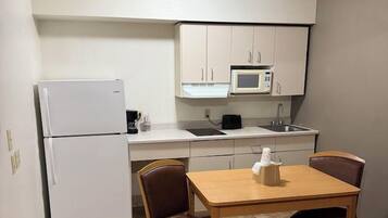 A compact kitchenette with a refrigerator, microwave, and sink. There is a small dining table with two chairs.