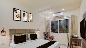 A hotel room with a bed, a desk, a chair, a TV, and artwork on the wall. - Classic Amar Resorrt (Motihari)