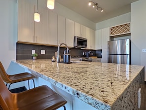 A modern kitchen with a granite countertop, stainless steel appliances, and a bar area with seating.