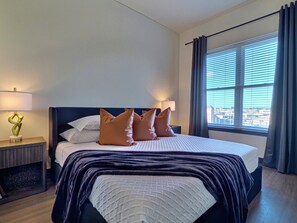 Una habitación de hotel con una cama grande, una mesita de noche con lámpara y una ventana con cortinas.