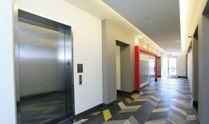 A modern hallway with an elevator, a red accent wall, and a patterned floor.