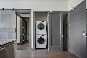 A laundry room with two stacked washing machines, a metal door, and a wooden floor.