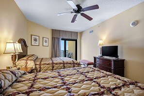 A hotel room with a bed, a television, a desk, a chair, a ceiling fan, and a window with curtains. - Anderson 1103 - Oceanfront 2BR Condo (Myrtle Beach)