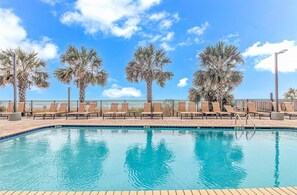 A pool with clear blue water, surrounded by palm trees and lounge chairs. - Anderson 1103 - Oceanfront 2BR Condo (Myrtle Beach)