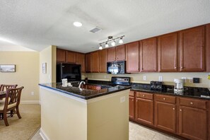 A kitchen with wooden cabinets, a granite countertop, a refrigerator, a microwave, and a toaster. - Anderson 1103 - Oceanfront 2BR Condo (Myrtle Beach)