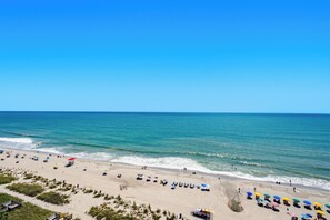 A beach with umbrellas and beach chairs, a clear sky, and the ocean. - Anderson 1103 - Oceanfront 2BR Condo (Myrtle Beach)
