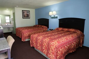 Habitación de hotel con dos camas, un escritorio, una silla, un espejo y una lámpara en la pared.