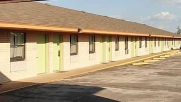 A row of motel rooms with individual doors and windows, a parking lot in front, and a clear sky.