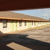 Filas de habitaciones de motel con puertas y ventanas individuales, un estacionamiento al frente y un cielo despejado.