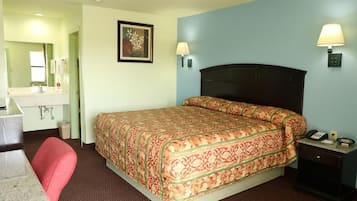 A hotel room with a bed, bedside table, lamp, and a desk with a chair.