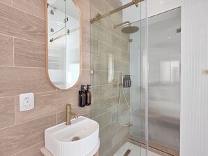 Ein modernes Badezimmer mit einem weißen Waschbecken, einer Duschkabine aus Glas und einem großen Spiegel.