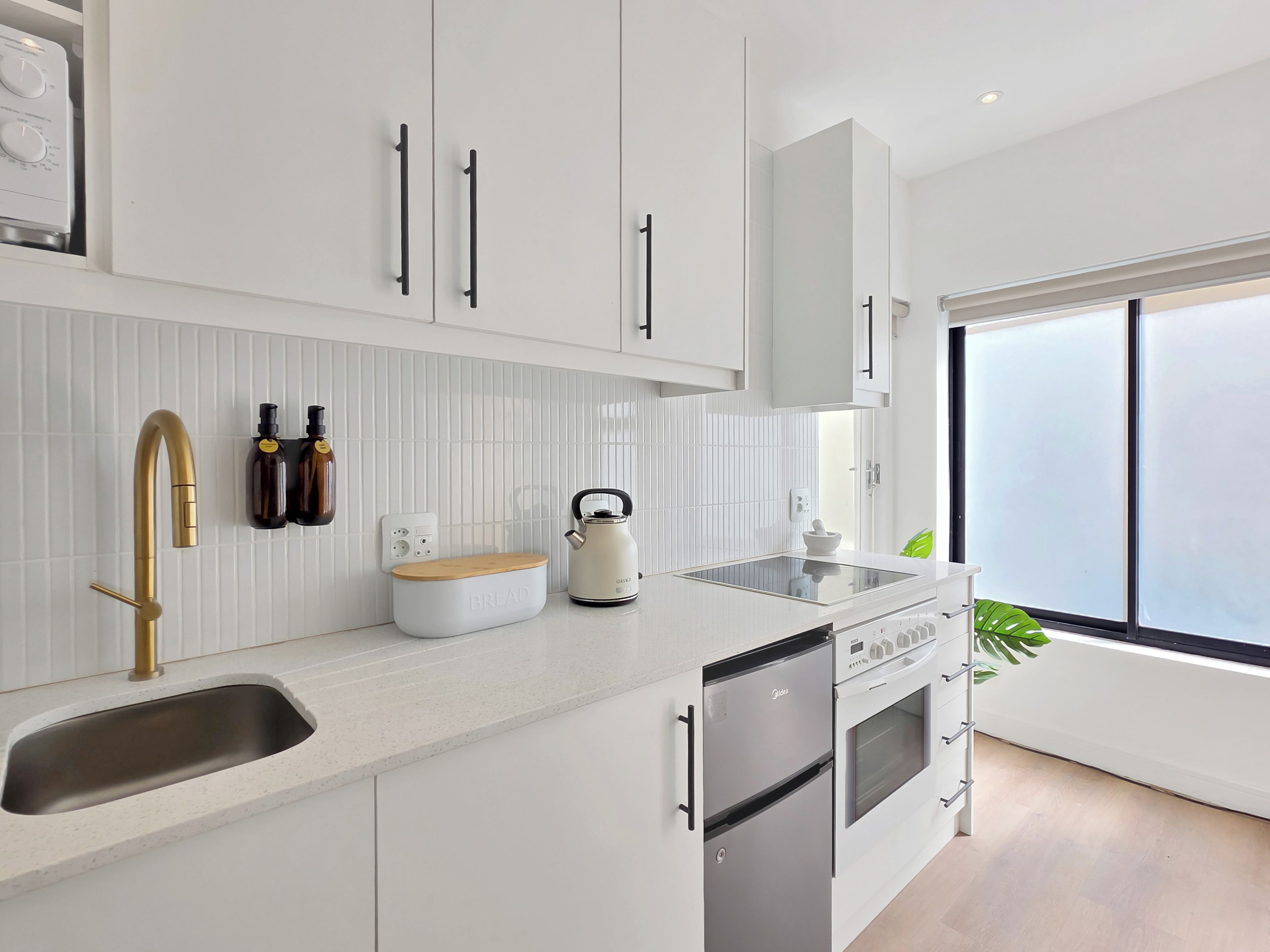 A modern kitchen with white cabinetry, a stainless steel sink, a kettle, and a built-in oven.