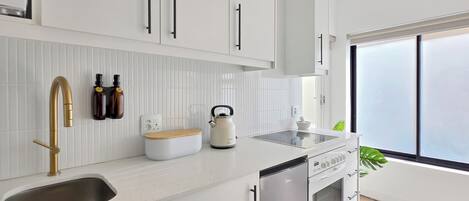 A modern kitchen with white cabinetry, a stainless steel sink, a kettle, and a built-in oven.