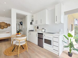 Cozinha moderna com armários brancos, área de jantar com mesa e cadeiras redondas e uma planta em vaso.