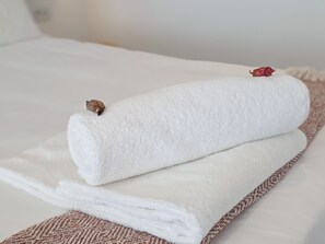 Toalha branca dobrada sobre a cama, com detalhe estampado na borda.