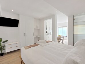 Ein modernes Schlafzimmer mit einem großen Bett, einem Nachttisch, einem Kleiderschrank und einem an der Wand befestigten Fernseher.