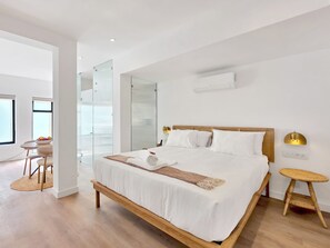 Ein modernes Hotelzimmer mit einem großen Bett, einem Nachttisch, einer Wand-Klimaanlage und Blick auf das angrenzende Zimmer.