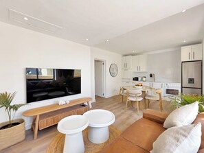 A modern living room with a flat-screen TV, a wooden bench, and a sofa. - One bedroom apartment with parking in Fresnaye (Cape Town)