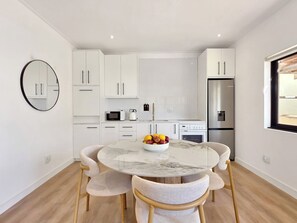 A modern kitchen with white cabinets, a round marble table, and a fruit bowl. - One bedroom apartment with parking in Fresnaye (Cape Town)