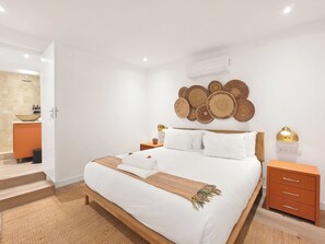 Une chambre à coucher comprenant un lit, des tables de chevet, un climatiseur fixé au mur et un élément décoratif mural.