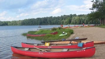 Canoes lined up on a sandy shore by a calm lake, with trees in the background.
