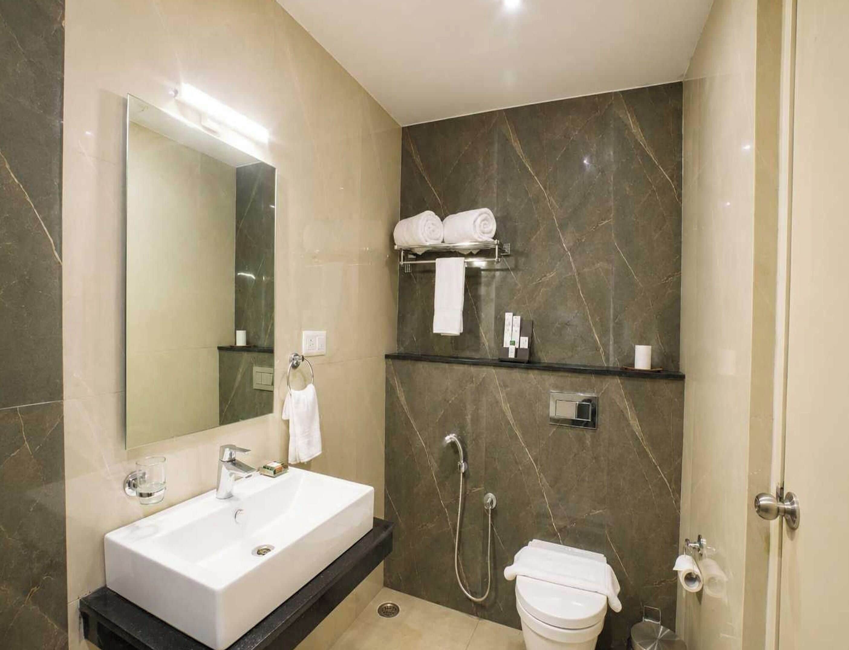 A modern bathroom with a large mirror, a sink, a shower, and a toilet.