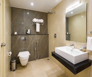 A modern bathroom with a white sink, a handheld showerhead, a toilet, and a towel rack. - Deluxe Twin Room Beacon Palette (Visakhapatnam)